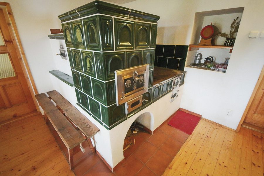 Zelená kachlová kamna s troubou a plotnou, dřevěná lavice